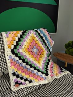 a crocheted granny blanket sitting on top of a couch next to a potted plant