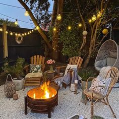 a fire pit surrounded by chairs and lights in a back yard with gravel flooring