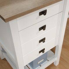 a white cabinet with three drawers and two doors on the bottom, in front of a wooden floor