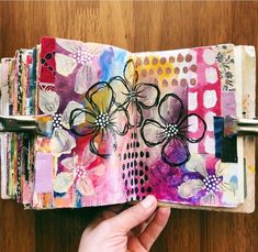 a hand holding an art journal with flowers on it, and the pages are covered in paper