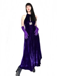 "a vintage 1960s 1970s long purple evening cocktail maxi dress  this elegant gown features a fitted bodice with peek-a-boo cut out, halter neckline , a beautiful open back, sleeveless and a long A-line skirt. the gown is made of a beautiful shade of deep purple soft velvet fabric . not lined. the dress is adorned with a stunning large brutalist silver tone metal embellishment . hook and eye closure at the back neckline. the perfect party dress this maxi dress is in near Mint Pristine vintage con Purple Maxi Dress For Prom Season, Purple Maxi Dress For Evening Prom, Purple Halter Neck Maxi Dress For Evening, Purple Halter Neck Maxi Dress For Party, Glamorous Fitted Purple Maxi Dress, Purple Velvet Party Dress, Purple Velvet Dress For Party, Glamorous Purple Evening Maxi Dress, Purple Maxi Evening Dress For Night Out