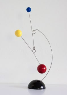 a metal sculpture with three different colored balls on it's head and two wires attached to the base