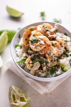 a white bowl filled with rice and shrimp on top of a table next to lime wedges