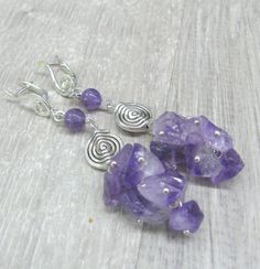 Extra long artisan earrimgs with natural amethyst crystal chips in a thick cluster. In one pair of earrings I combines several shapes: gemstone chips, disc with a spiralpattern and silver swirls looking a little like music symbol - G clef. Length: 78 mm or 2.75 inches from ear holeto the bottom. Amethyst cluster - 25 mm long and 16 mm wide. Amethhyst round bead: 6 mm Round silver plated disc bead with spiral pattern: 11 mm. G clef shaped earring top: 17 mm. I have a matching necklace available h Silver Amethyst Dangle Crystal Earrings, Silver Amethyst Dangle Earrings, Silver Amethyst Wire Wrapped Earrings, Silver Amethyst Crystal Earrings With Ear Wire, Nickel-free Silver Amethyst Crystal Earrings, Silver Amethyst Crystal Earrings As Gift, Silver Amethyst Crystal Earrings For Gift, Lavender Amethyst Earrings With Natural Stones, Romantic Gifts For Girlfriend