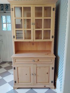 a wooden china cabinet with glass doors on the top and bottom, against a checkered wall