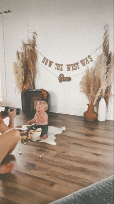 a woman taking a photo of a baby sitting on the floor in front of her