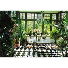 a room filled with lots of potted plants next to a table and chairs in front of large windows