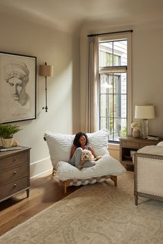 a woman sitting on top of a white couch in a living room next to a window