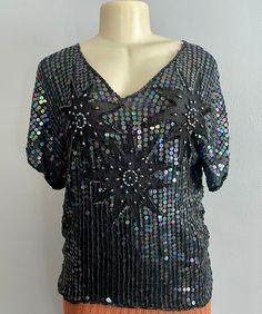 "Vintage 70s Sequins Silk Blouse by Sarafino. Made in India, this silk top features a floral aabstract design made with sequins and long beads over a black background.  CONDITION: It's missing some sequins on top of one of the shoulders which is reflected in the price. No size label. Estimated size: L Approx Flat Measurements:  Bust: 40\" Waist: 38\"  Length: 25\" Most of our pieces are pre-loved vintage or antique items. They will sometimes have some wear as they are at least 20 years old. Plea Festive V-neck Top For Party Season, Festive Sequined V-neck Top, Festive V-neck Sequin Top, Retro V-neck Party Tops, Disco Style Top For Evening Party Season, Festive Black V-neck Top, Black Tops For Festive Party Season, Black Sequined Summer Blouse, Glamorous Silk Top With Sequins