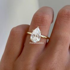 a woman's hand with a yellow gold ring and a pear shaped diamond on it