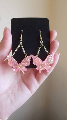 a pair of pink butterfly dangle earrings on a black display stand in someone's hand