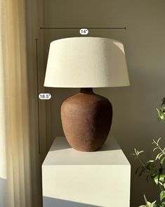 a large brown vase sitting on top of a white block next to a lamp shade