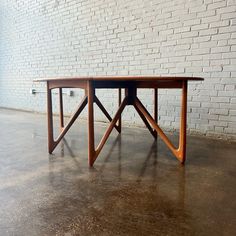 a wooden table sitting on top of a cement floor next to a white brick wall