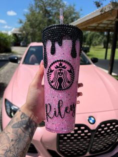 a person holding up a pink starbucks cup in front of a pink car with the word kleen on it