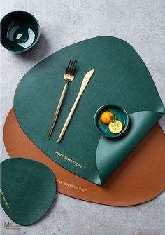 a place mat with food on it and utensils next to the plate that has an orange in it