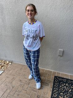 a woman standing in front of a wall wearing plaid pants and a t - shirt that says junior jewels