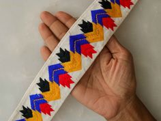 a hand holding a white ribbon with red, yellow and blue designs on it's side