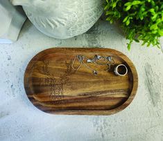 a wooden tray with jewelry on it next to a potted plant