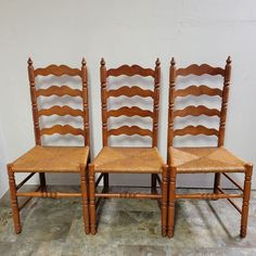 three wooden chairs sitting next to each other on a tile floor in front of a white wall