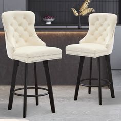 two white barstools with black legs in front of a counter and bar stools