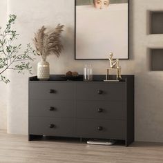 a black dresser in a white room with a painting on the wall and vases