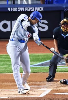 a baseball player swinging a bat at a ball during a game on the field with another player behind him