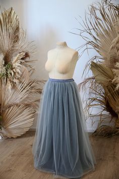 a mannequin wearing a blue tulle skirt in front of some dried plants