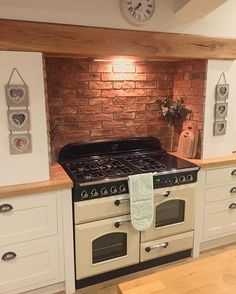 an old fashioned stove in a kitchen with white cabinets and brick wall behind the oven