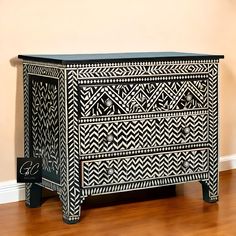 an ornate black and white chest of drawers in a room with hard wood flooring