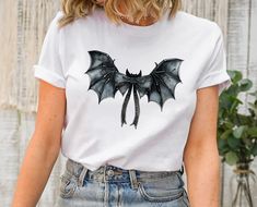 Halloween Bat Shirt, Black Bat Bow Tee , Cute Halloween Bow Tee, Spooky Gothic Bow, Halloween Women Shirt, V neck TShirt Gift Hi , I'm Eliza. Welcome to my shop! Your precious shirt is here. As a small business owner making happy  my customers with their purchase is my priority. I prepare all my shirts with love. Please don't hesitate to contact me if you have any question ,concern ,compliment or just to say hi:) Thanks for supporting me. Please check all details about your order below! BRANDS: Punk Halloween Cosplay Tops, White Halloween Cosplay Top, Punk Style Tops For Halloween Cosplay, Punk Tops For Halloween Cosplay, White Top For Halloween Cosplay, Grunge Halloween Cosplay T-shirt, Halloween Cosplay Short Sleeve T-shirt, Edgy Halloween Cosplay T-shirt, Gothic Cosplay T-shirt For Halloween