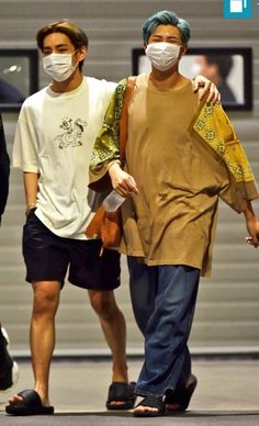 two men walking down the street wearing face masks