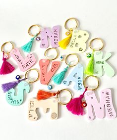 many different key chains with tassels and name tags attached to them on a white surface