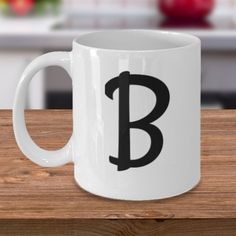 a white coffee mug with the letter b on it sitting on a wooden table in front of a kitchen