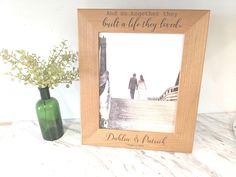 a wooden frame with a couple walking on a dock and flowers in a vase next to it