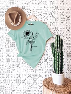 a t - shirt hanging on a wall next to a cactus and a cowboy hat