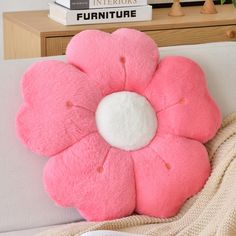 a pink flower pillow sitting on top of a white couch next to a stack of books