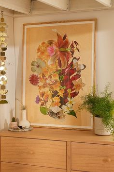 a painting hanging on the wall next to a dresser with flowers and plants in it