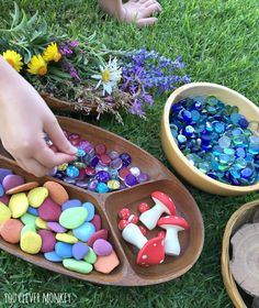 children playing with colorful rocks and stones in wooden trays on the grass next to flowers