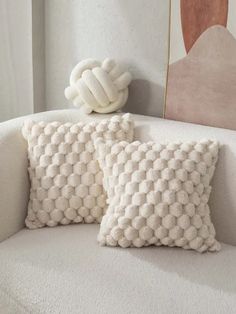 two white pillows sitting on top of a couch next to a pillow with a knot