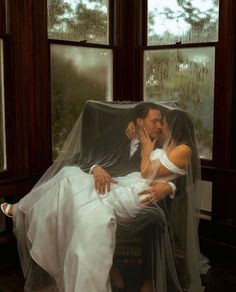 a bride and groom sitting on a chair in front of a window covered by a veil