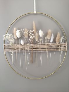 a circular metal rack with dried flowers on it hanging from the wall in front of a gray wall