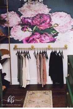 a closet with clothes hanging on the wall and a floral painting above it, along with a rug