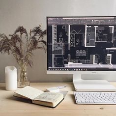 a computer monitor sitting on top of a desk next to a book and vase filled with flowers