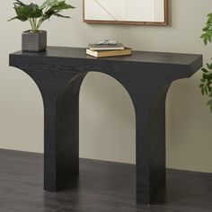 a black console table with two plants on top and a framed photograph above it, along with a pair of eyeglasses