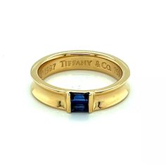 An elegant and authentic stack ring from Tiffany & Co. It is crafted from 18k yellow gold with a polished finish and features a 4.5mm wide concave design around the entire band with two channel set baguette sapphires.  It is signed by the designer with the gold content.    Brand:   Tiffany & Co.  Hallmark:  1997 Tiffany & Co. 750  Sapphire: 0.30ct  Material:  18k yellow gold  Measurement:  0.19" wide x 0.11" high  Ring Size:  6  Weight: 5.8 grams Luxury Baguette Cut Stackable Promise Rings, Luxury Emerald Cut Ring With Channel Set, Designer Polished 14k Gold Rings, Designer 14k Gold Rings With Polished Finish, Luxury Emerald Cut Channel Set Ring, Luxury Princess Cut Ring With Channel Set, Luxury Baguette Cut Stackable Rings For Formal Events, Luxury Baguette Cut Stackable Rings For Formal Occasion, Luxury Wide Band Stackable Rings For Anniversary