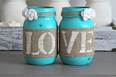 two mason jars with love painted on them sitting on a table next to white flowers