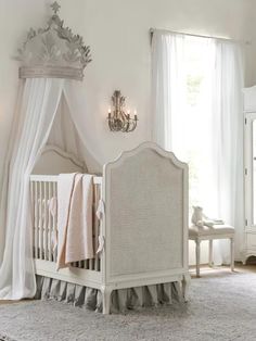 a white crib in a room with curtains and chandelier