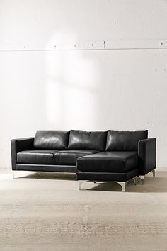 a black leather couch sitting on top of a wooden floor next to a white wall