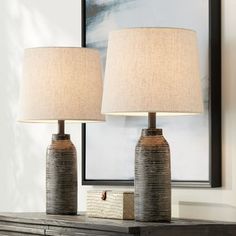 two lamps sitting on top of a wooden table next to a framed painting and lamp shade