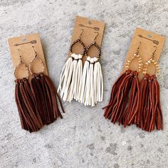 three pairs of tasseled earrings are shown on the ground with tags attached to them